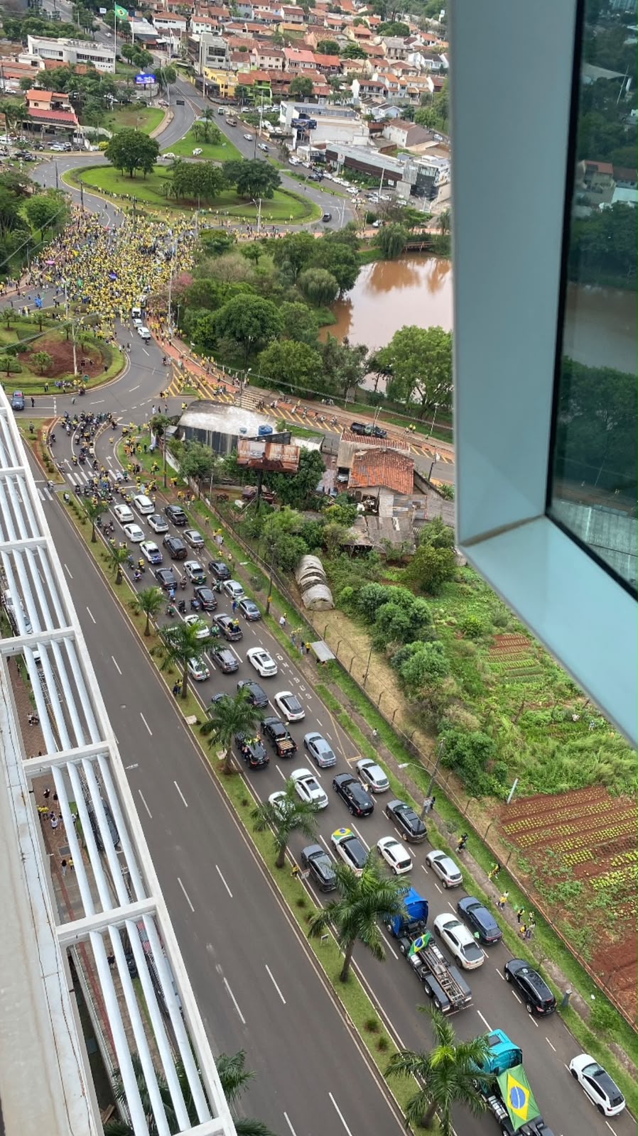 Vista do alto de um prédio mostra concentração de manifestantes de verde e amarelo numa rotatória e uma fila de carros e caminhões na avenida