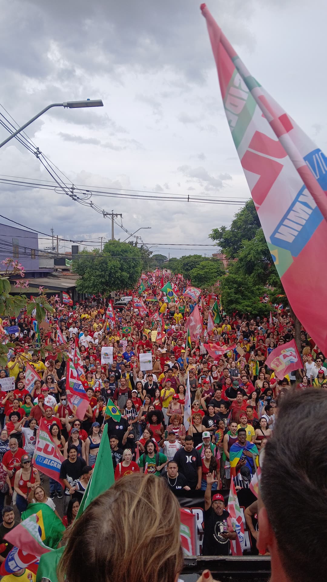 Multidão vestida de vermelho ocupa a Avenida Saul Elkind, em Londrina, com bandeiras de Lula e do Brasil, vista do alto do trio
