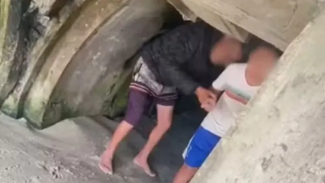 Uma cela de prisão escura e confinada com um catre gasto. A luz é fraca e projeta sombras longas.