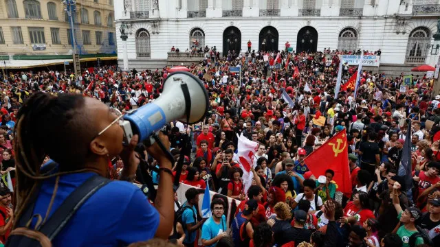 Grupo de estudantes universitários reunidos em praça pública com faixas sobre educação e democracia.