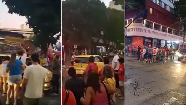 Um carro amarelo avançando em direção a uma multidão de pessoas em uma rua de cidade, com faixas e cartazes ao fundo.