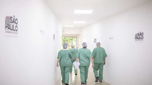 Representação de identidade médica falsa e estetoscópio sobre mesa, com fundo de hospital desfocado