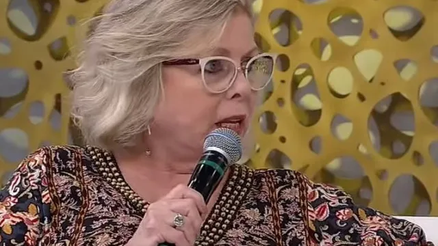 Uma mão segurando um microfone antigo em um palco com luz baixa, representando o mundo do entretenimento.