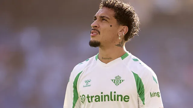 Jogador em repouso no banco de reservas de um estádio, segurando a perna com dificuldade