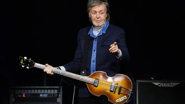 Músico em estúdio escuro com instrumentos vintage, em postura reflexiva e introspectiva, com iluminação quente
