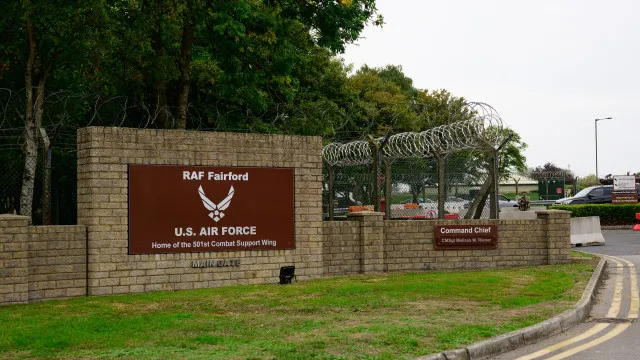 Perímetro de segurança de uma base aérea militar ao amanhecer, com cercas, barreiras, veículos de emergência e luzes piscantes