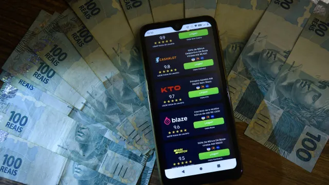 Uma mão segurando um smartphone com a tela de um aplicativo de apostas, com documentos jurídicos e um martelo de juiz desfocados ao fundo.