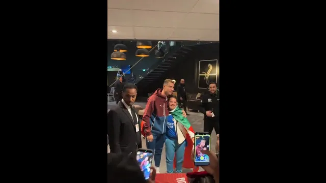 Craque de futebol cercado por crianças em hall de hotel, assinando autógrafos e sorrindo