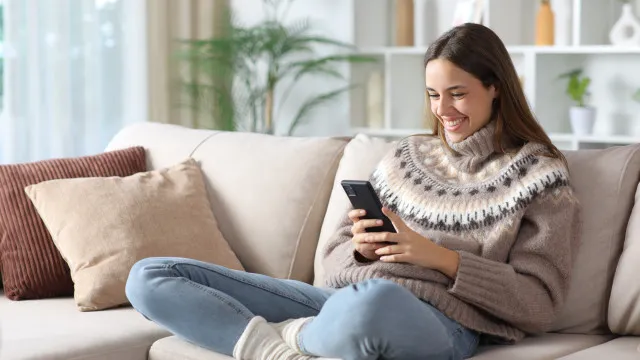 Uma mão segura um smartphone moderno com a tela iluminada, exibindo ícones de aplicativos.