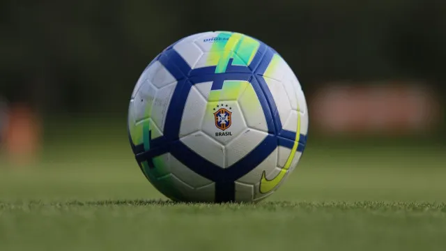Estádio de futebol iluminado à noite, com o gramado em destaque e arquibancadas vazias, transmitindo a atmosfera de um jogo importante.