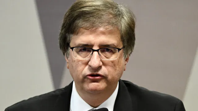 Sala de tribunal ou conselho com mesa formal, documentos espalhados e iluminação natural, ambiente institucional