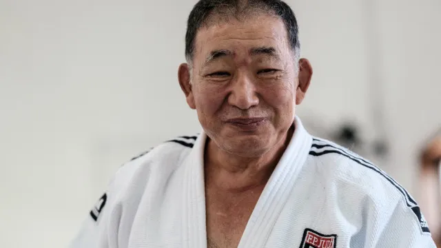 Um kimono de judô dobrado sobre um piso de madeira, com uma medalha de bronze em cima, iluminado por uma luz suave.