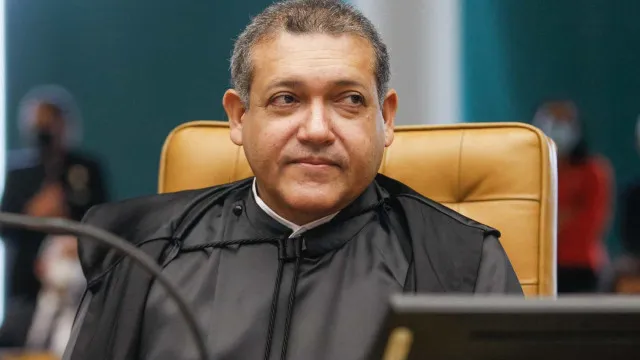 Uma mão segurando um smartphone com o logo de um aplicativo de mídia social, com pessoas interagindo em um fórum digital ao fundo.