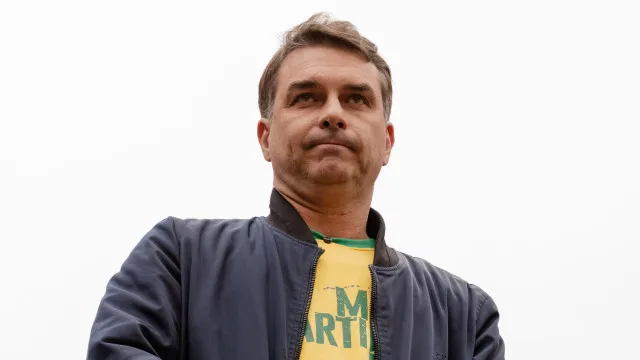Uma mão segura um maço de dinheiro, com documentos oficiais desfocados ao fundo, sugerindo transações financeiras e burocracia.