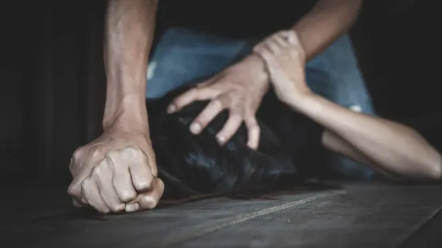 Um distintivo de polícia sobre uma mesa, ao lado de um bloco de notas e uma caneta, com um corredor escolar desfocado ao fundo.