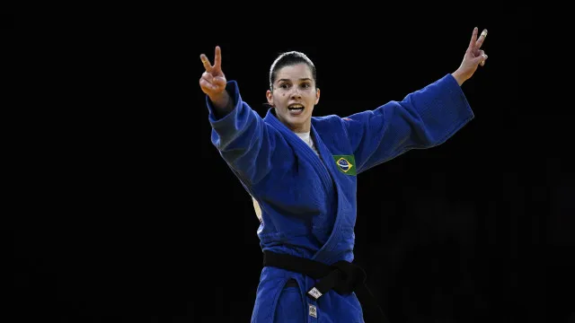 Dois judocas em uniforme branco durante uma luta em competição internacional, em tatame azul