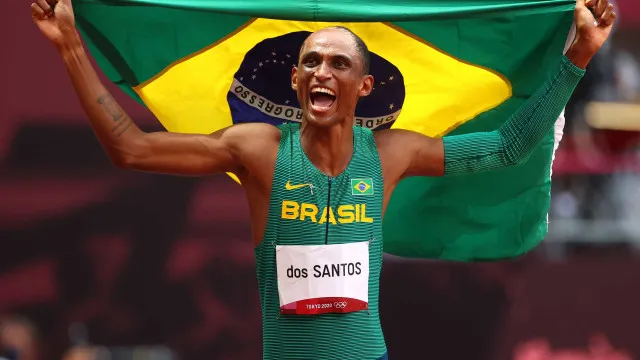 Silhueta de um atleta cruzando a linha de chegada em uma pista, com público ao fundo.