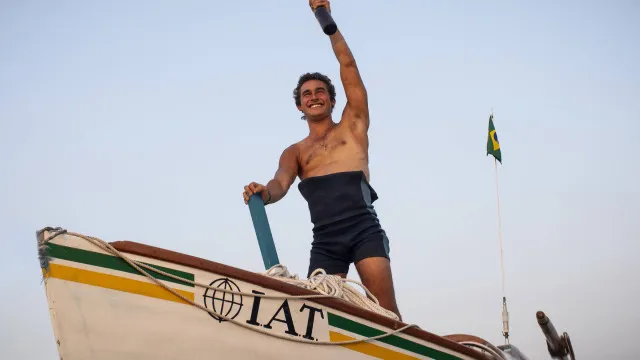 Homem remando sozinho em barco pequeno no meio do oceano infinito durante o amanhecer