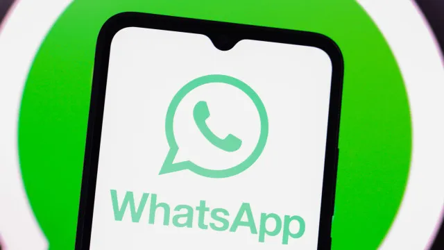 Uma mão segurando um smartphone com o WhatsApp aberto, exibindo a tela de agendamento de mensagens com ícones de calendário e relógio.