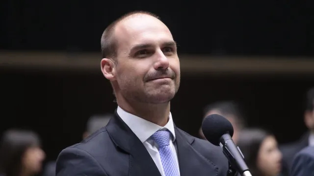 Uma silhueta escura de um político discursando em um púlpito, com microfones e iluminação dramática.