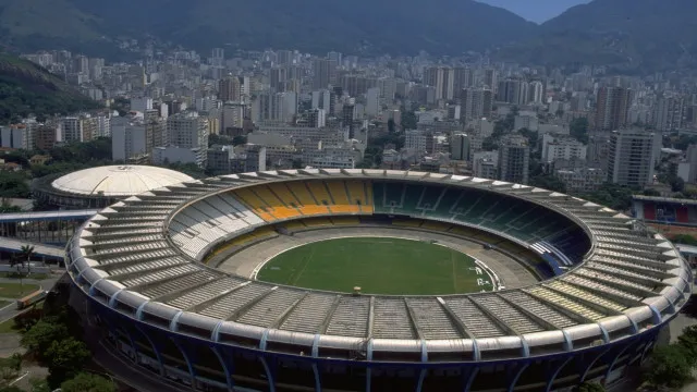 Um estádio de futebol vazio ao anoitecer, com os holofotes acesos, mostrando a grandiosidade da estrutura.